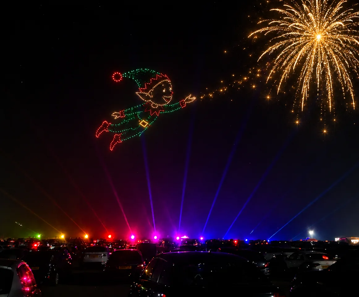 Drive-in cars watching a drone elf and a golden firework in the night sky